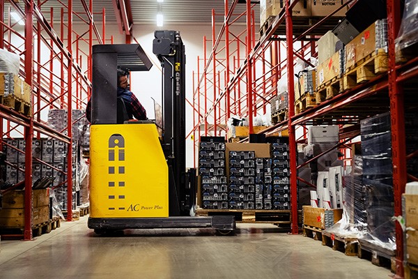 Forklift operating in warehouse collecting pallet of computers from a shelf